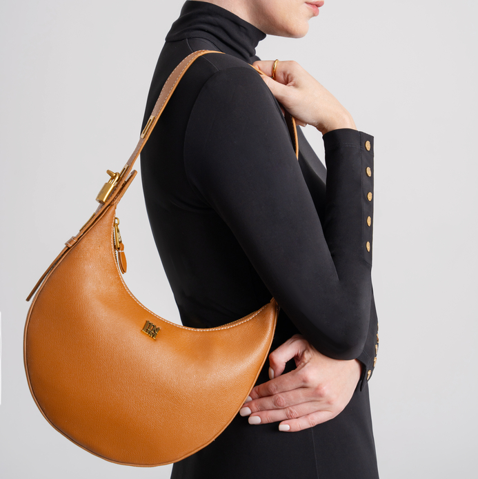 Brown leather crescent shoulder bag worn by woman in black outfit, classic minimalist hobo bag with structured shape for everyday elegance