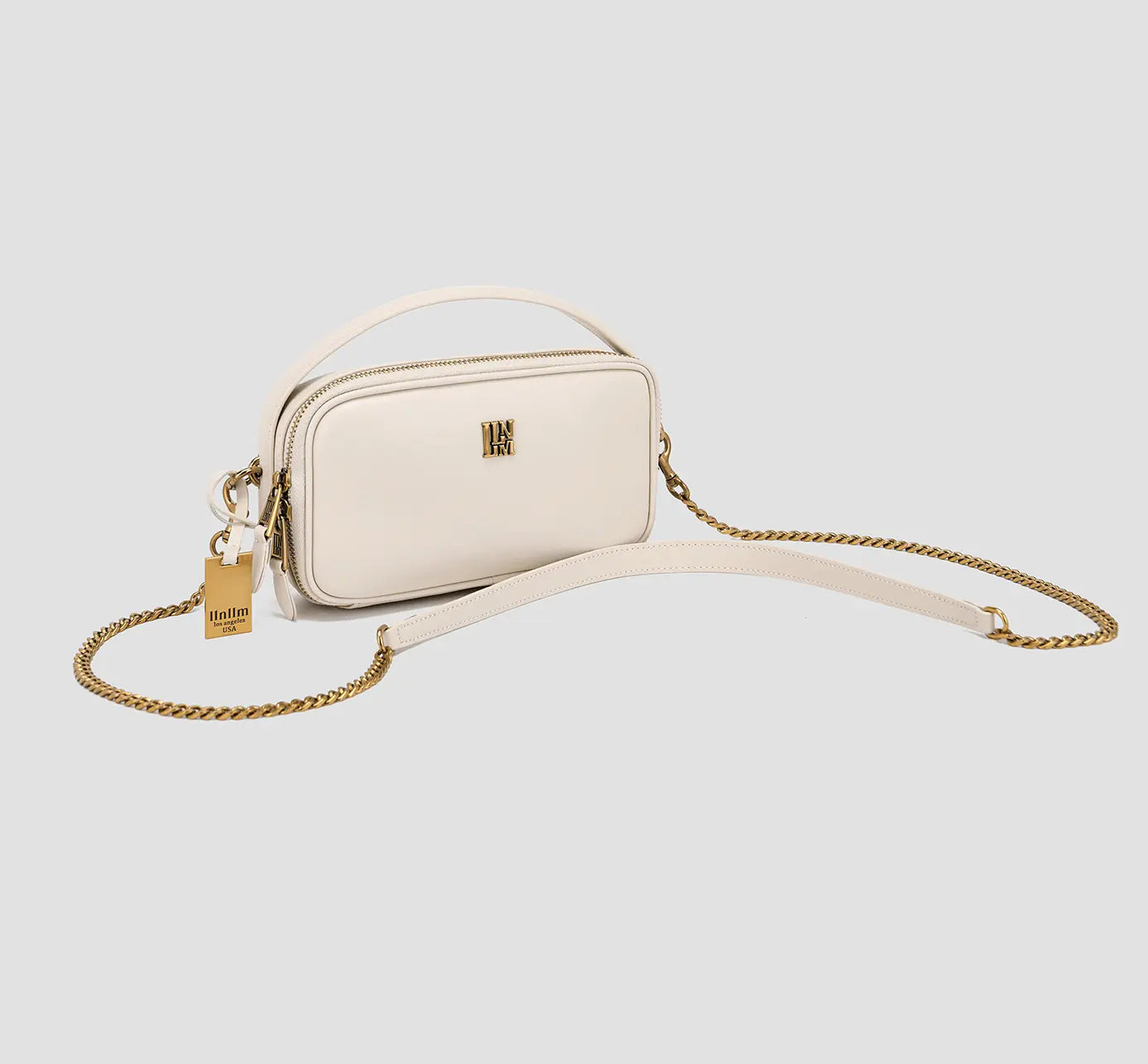 This is an angled view of a chic white compact crossbody bag for women with a gold chain strap — a minimalist square mini-shoulder bag.