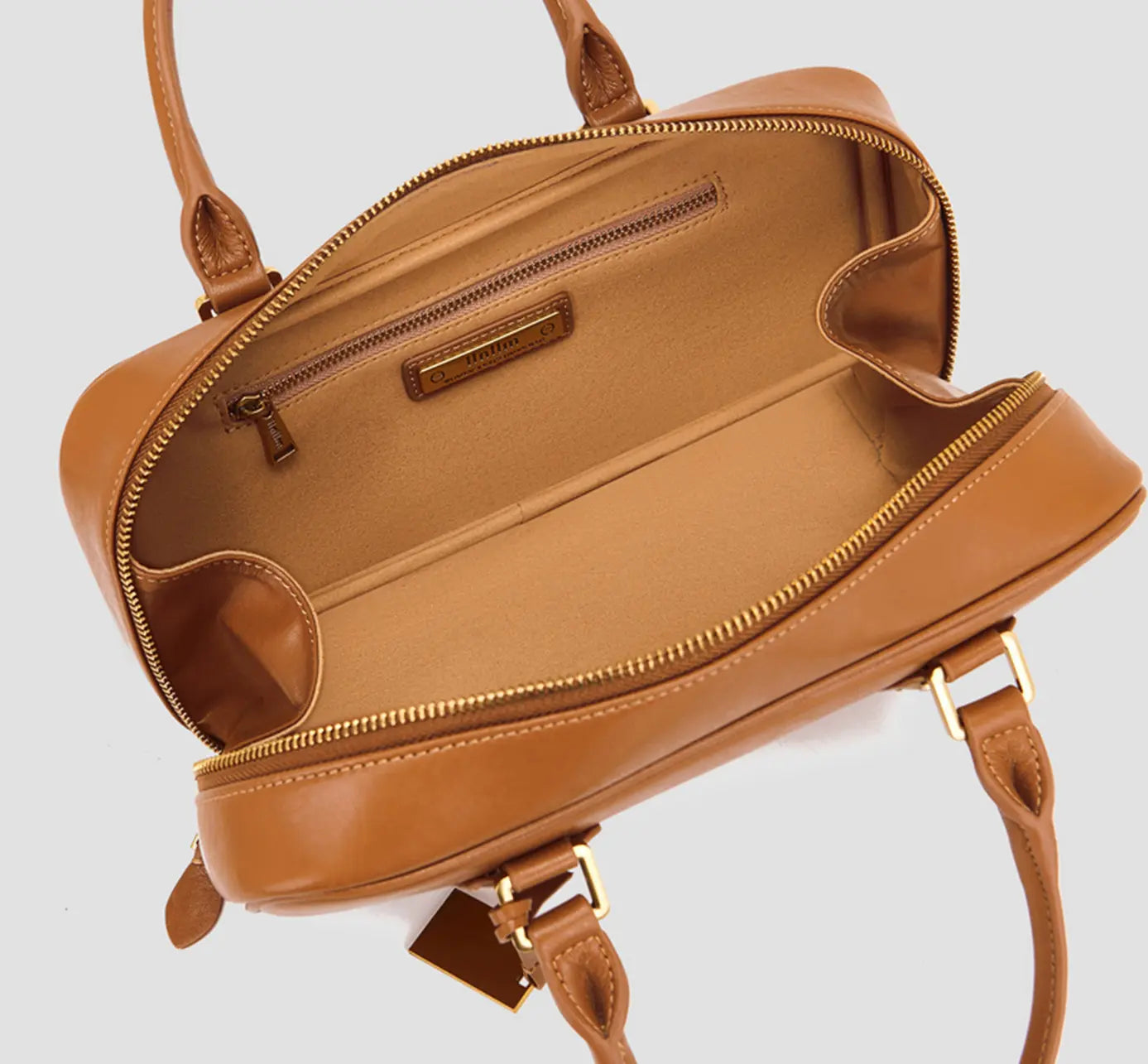 The spacious interior of tan leather handbag with zippered pocket and logo tag.
