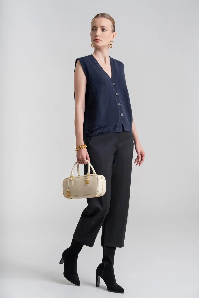 Woman in dark vest and trousers holding a white leather square top handle crossbody bag.