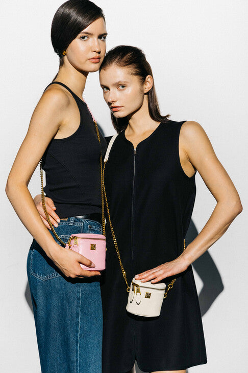 Models wear llnllm pink and cream mini leather crossbody bags with gold chain straps, styled with black outfits for a chic, minimalist street look.