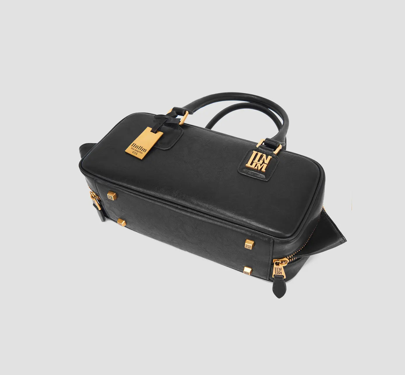 The angled bottom of black handbag with gold protective feet and side zipper detail.
