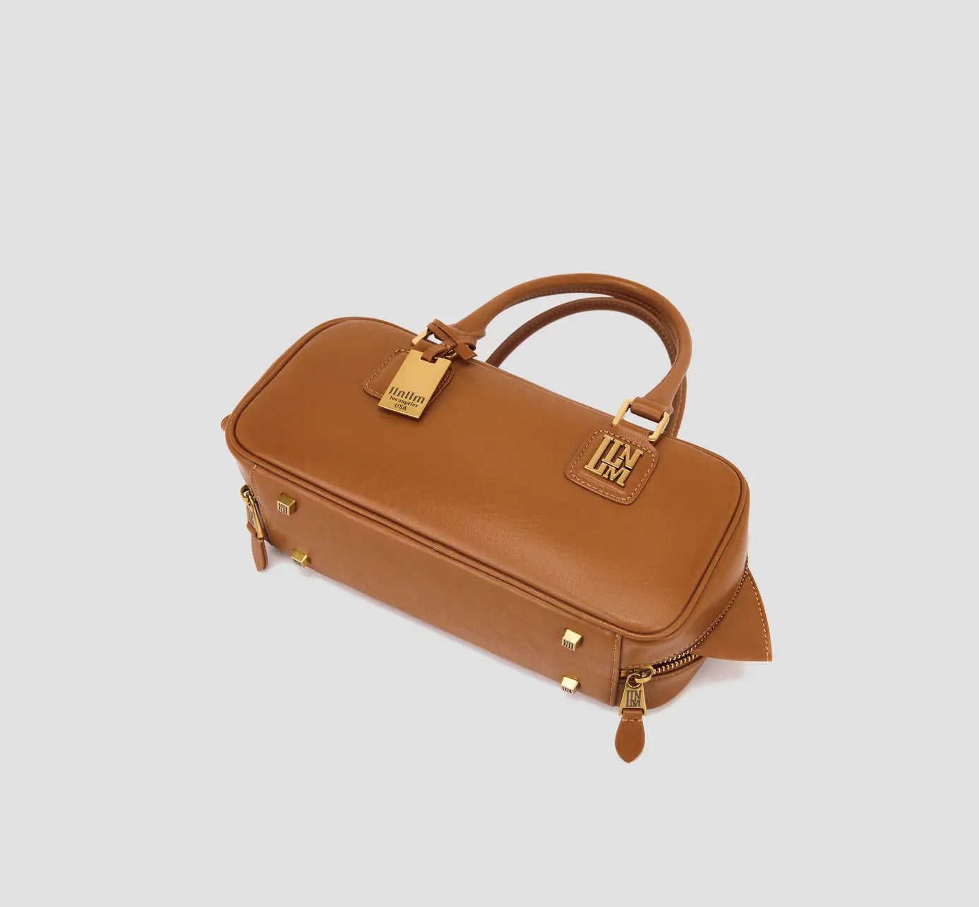 The bottom view of caramel handbag with logo-stamped metal feet and zipper details.