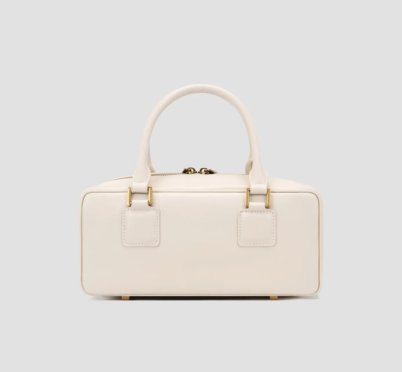 The back view of minimalist white leather handbag with top handles and gold loops.
