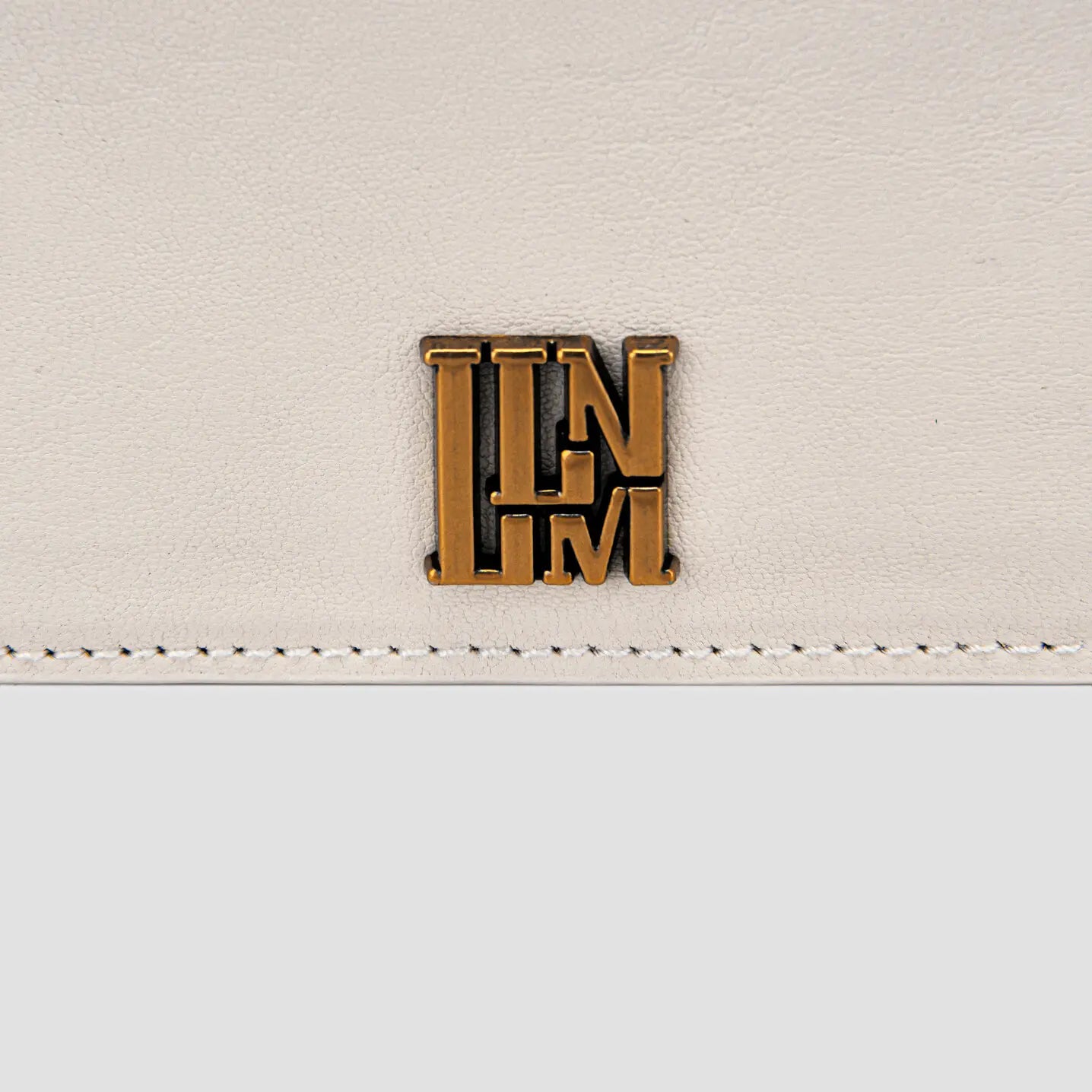 Close-up of  gold logo on white slim leather card holder.