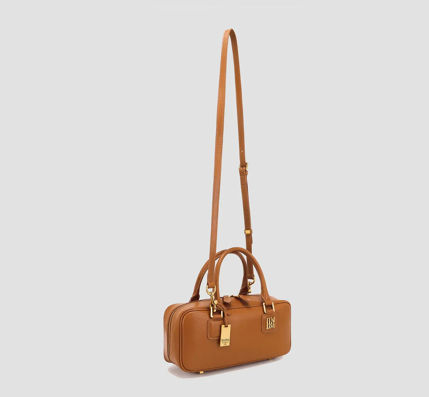 The Angled view of Caramel brown leather handbag with detachable long strap and gold accents.