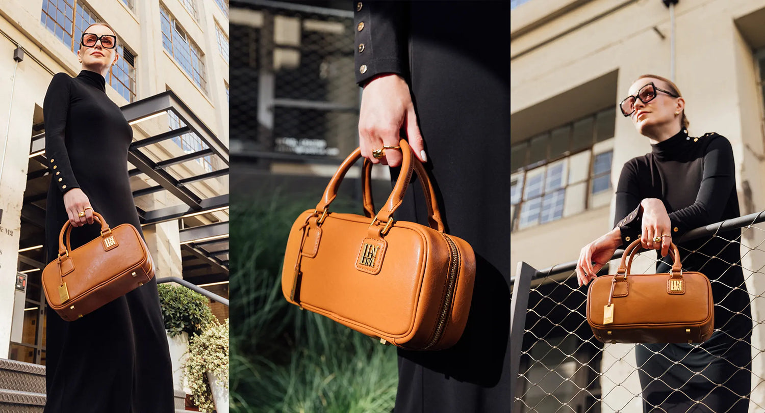 A woman holding a leather brown top handle designer bag in front of a modern industrial building, this purse urban expression is also a satchel small handbag.