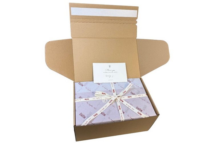 Opened box showing wrapped handbag with ribbon and thank-you card.